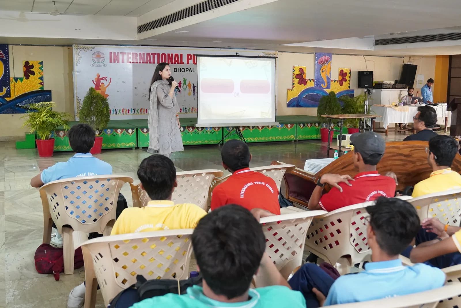 A facilitator speaking beside a presentation screen in a school hall