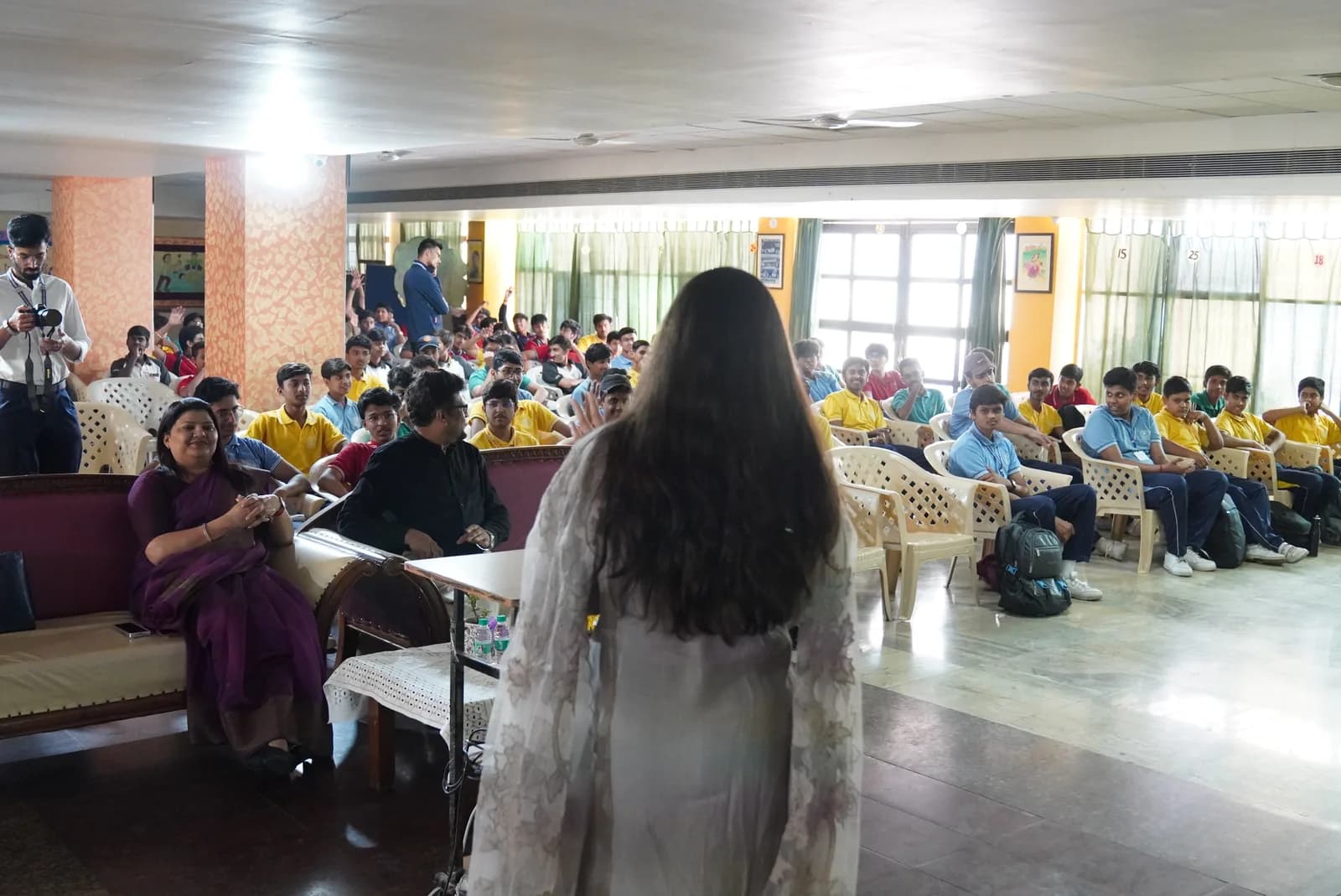 A facilitator addressing students seated in a school hall