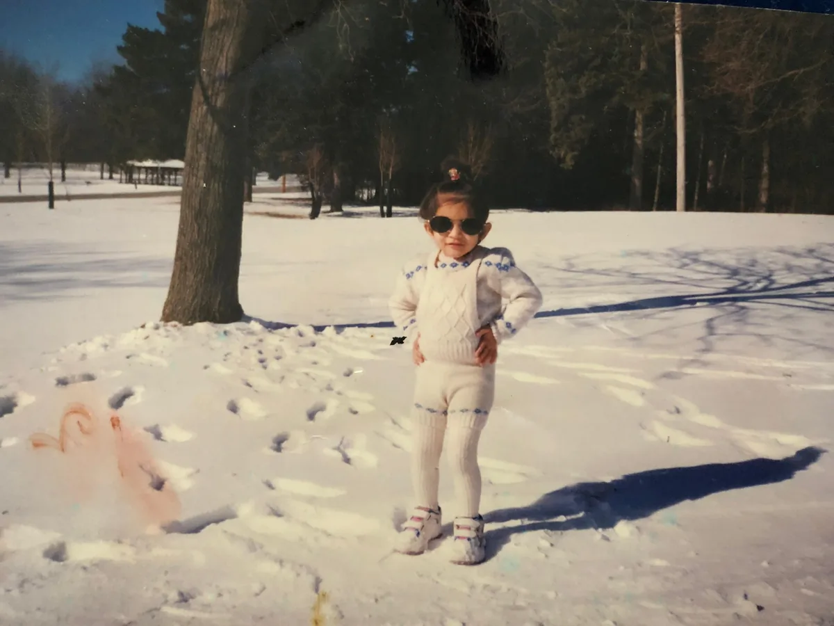 A toddler standing in the snow beside a tree
