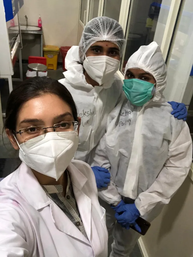 Riddhi Jain in a face mask beside two colleagues in full protective suits