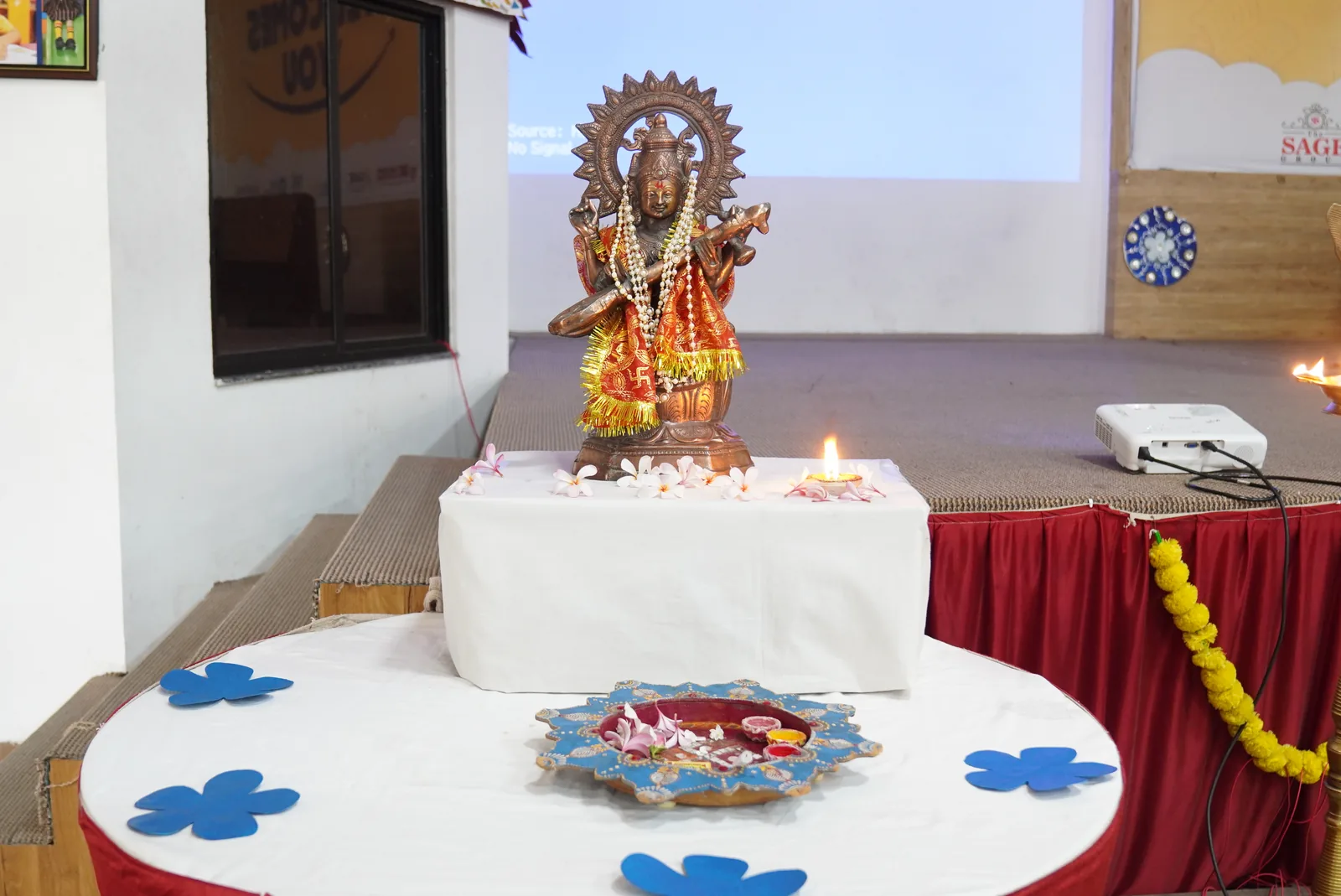 A brass lamp, flowers, and a garlanded idol set out on a draped table