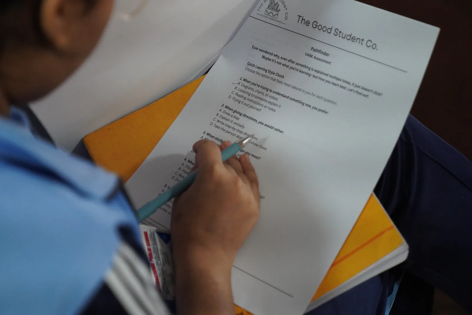 A student writing answers on a printed The Good Student Co. worksheet